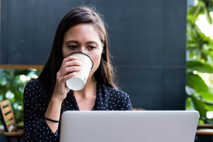 Mujer navegando en un equipo portátil y tomando café