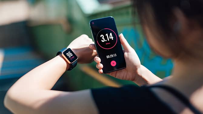 Una mujer que usa una aplicación para la actividad física en su smartphone y reloj inteligente. Las aplicaciones de seguimiento de la actividad física son un ejemplo de los posibles beneficios de la tecnología en la salud