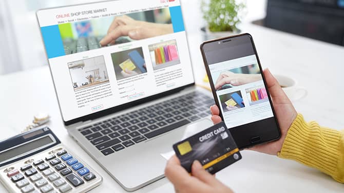 Casi todas las actividades online pueden contribuir a la huella digital. La imagen muestra a alguien sosteniendo su teléfono y su tarjeta de crédito frente a la pantalla de un ordenador con una ventana de compras online abierta.